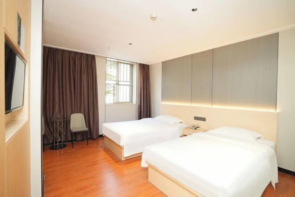 Une chambre d’hôtel avec deux lits, un bureau, une chaise, une télévision et une fenêtre avec des rideaux.
