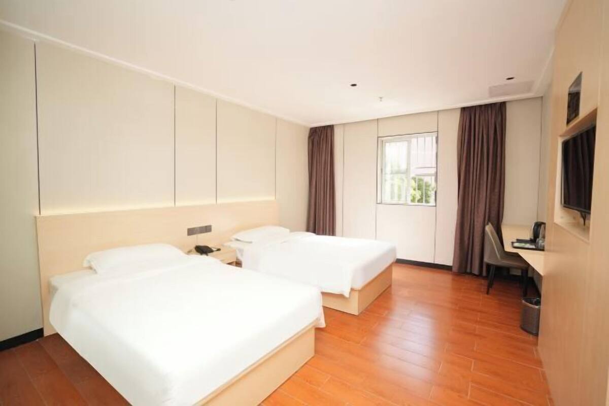 Une chambre d’hôtel avec deux lits, un bureau, une chaise, une télévision et une fenêtre avec des rideaux.