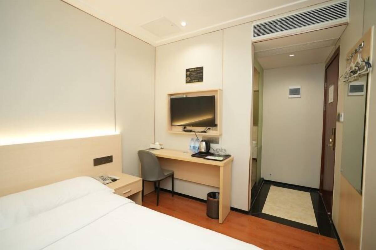 Une chambre d’hôtel comprenant un lit, un bureau avec une chaise, une télévision et une petite poubelle.