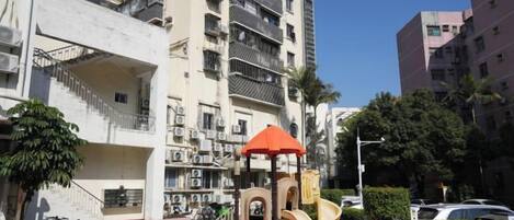 A multi-story residential building with balconies, a playground, and a clear sky.