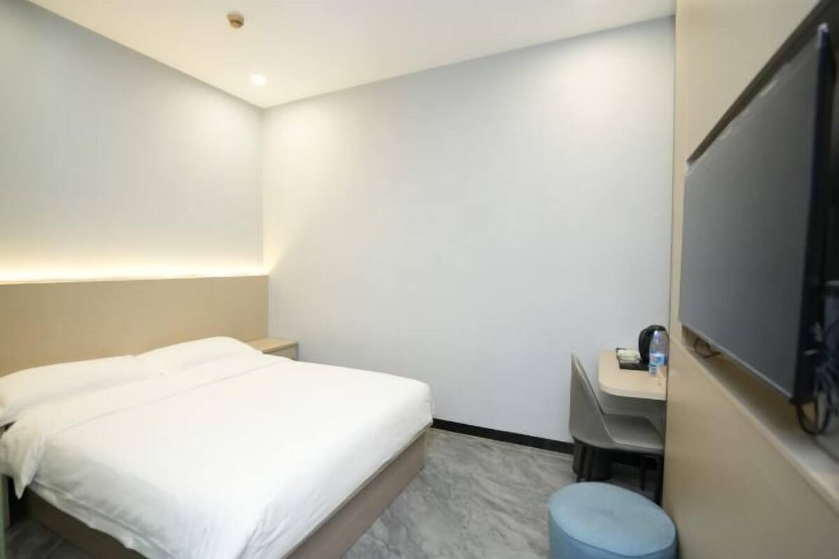 Une chambre d’hôtel équipée d’un lit, d’un bureau, d’une chaise, d’une télévision et d’un petit tabouret.