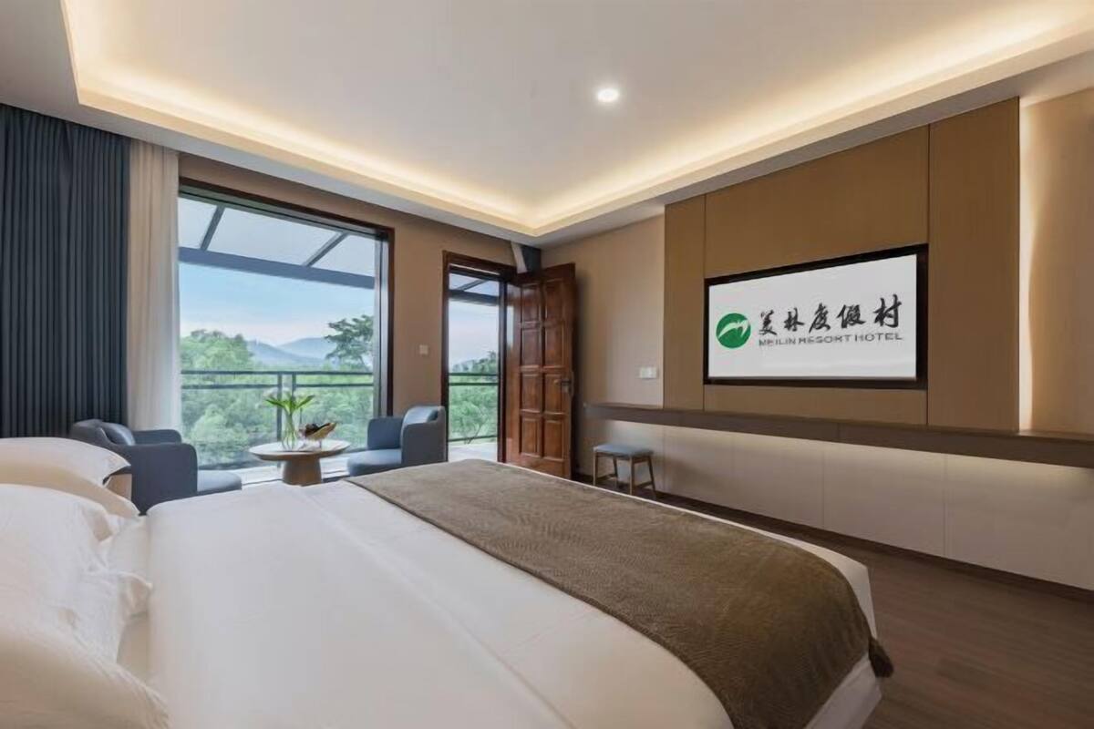 Quarto de hotel moderno com uma cama grande, uma TV fixada na parede e uma varanda com vista para o verde.