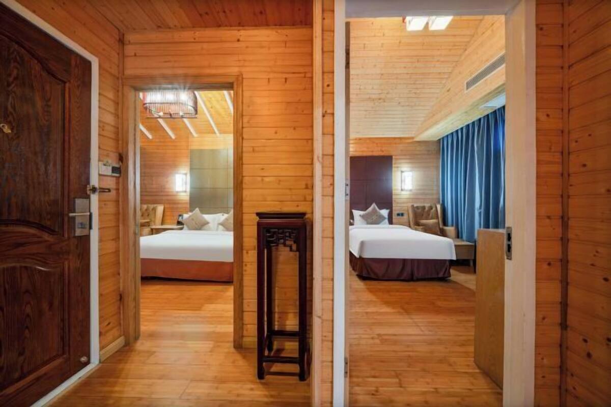 Interior de madeira com duas camas, uma mesinha e uma porta.