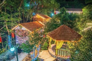 A treehouse with a thatched roof, surrounded by lush greenery and illuminated by string lights. - Anji Meilin Resort (Anji)