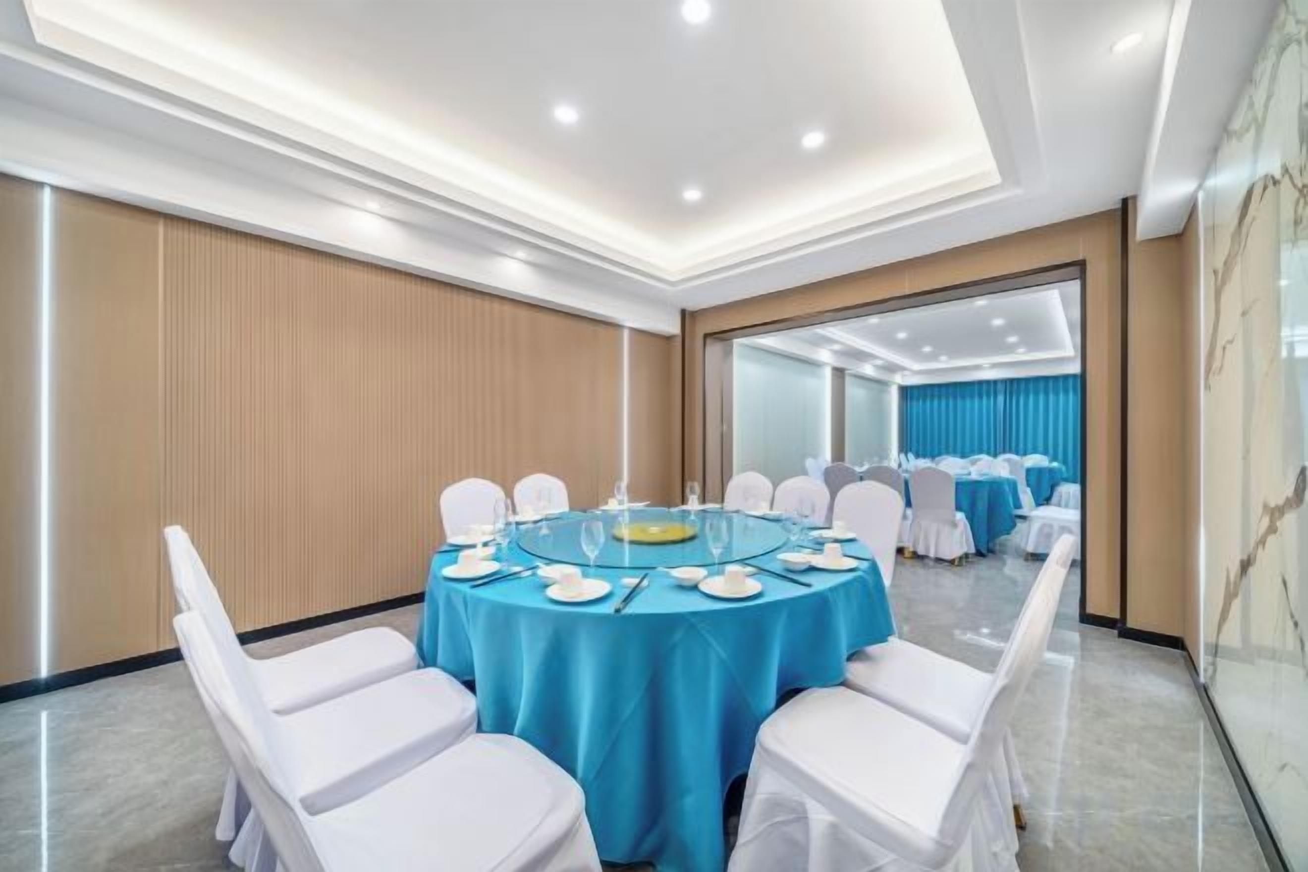 A conference room with a round table, white chairs, and a blue tablecloth.