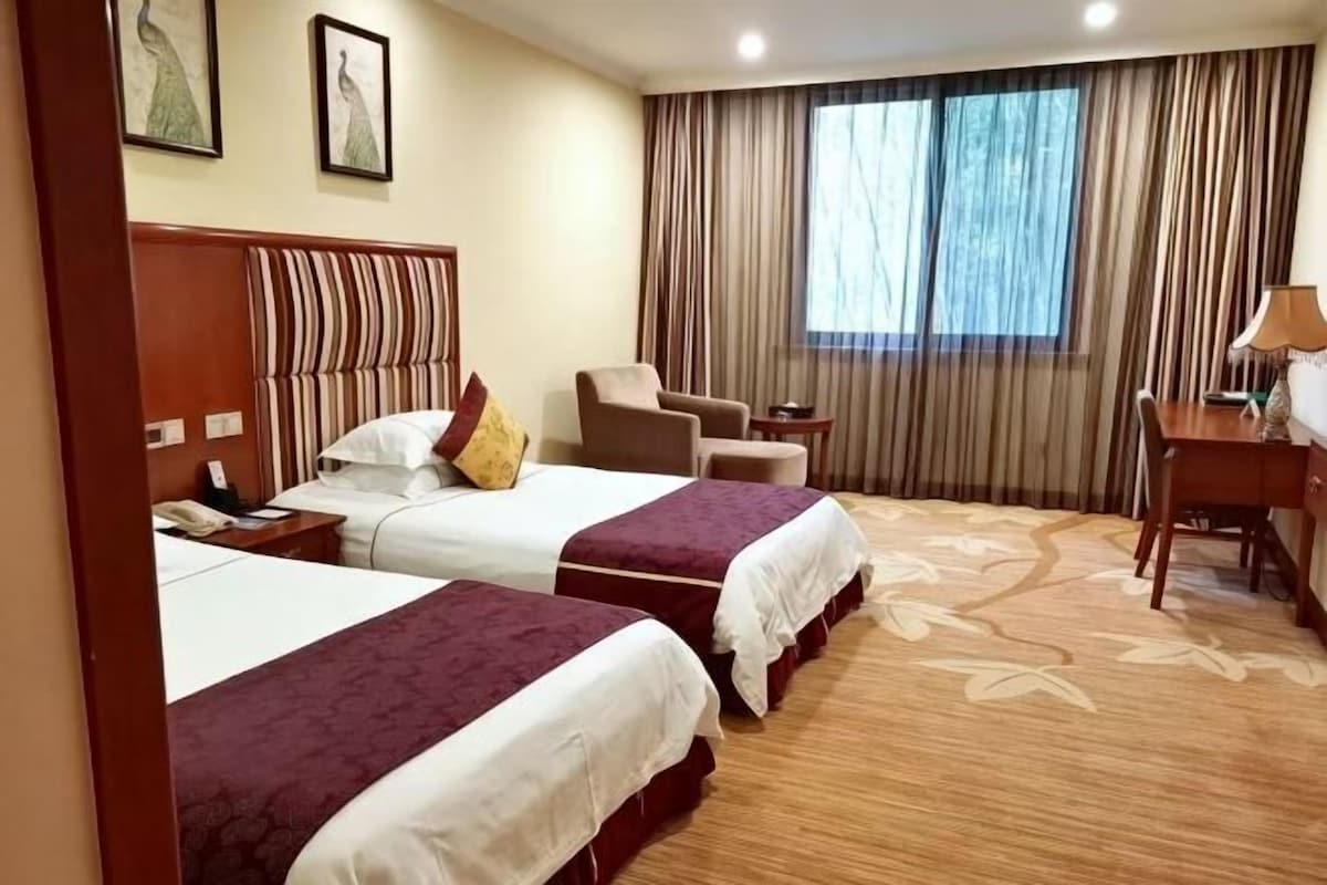 Habitación de hotel con dos camas, un escritorio, una silla y una ventana con cortinas.