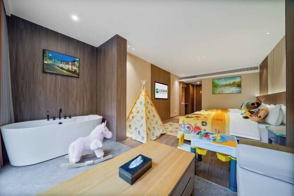 Quarto de hotel moderno com uma banheira grande, área de recreação com brinquedos, uma tenda e uma cama com travesseiro infantil.