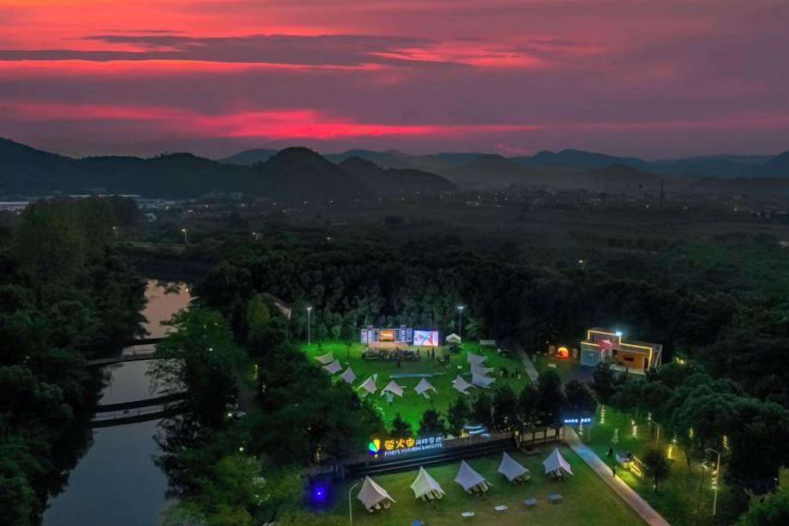 Un camping con tiendas de campaña, un edificio iluminado y un río.