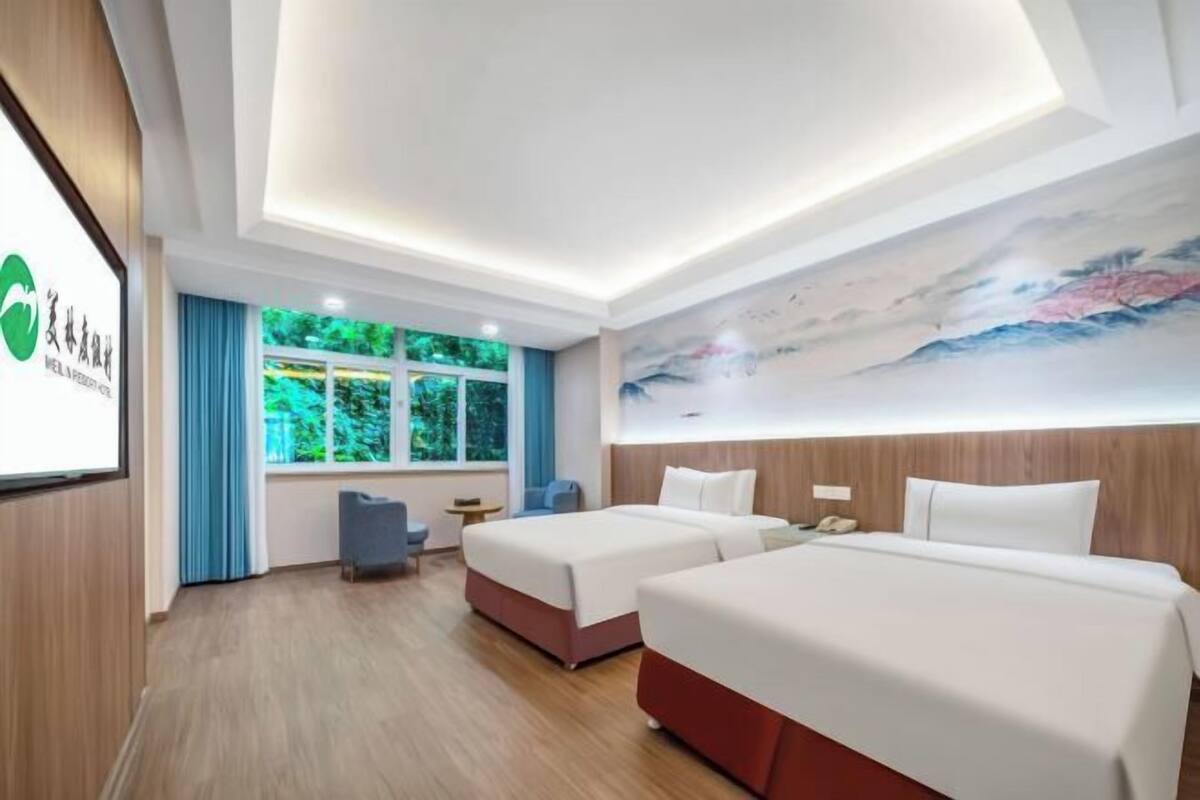 Quarto de hotel com duas camas, uma escrivaninha, uma cadeira, uma janela com cortinas e um quadro na parede.