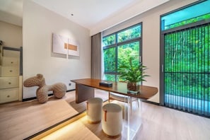 A modern room with a wooden desk, two stools, a potted plant, and a large window with a view of greenery. - Anji Meilin Resort (Anji)