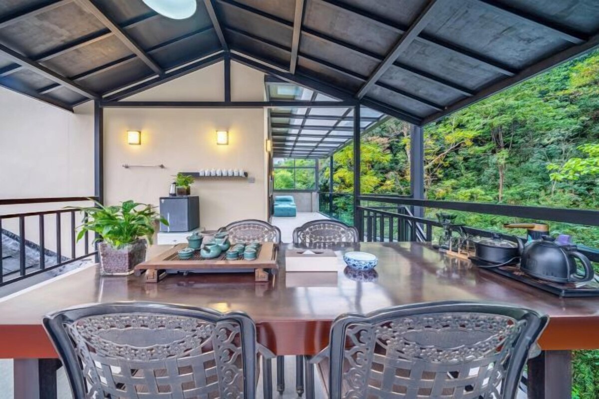 An outdoor dining area with a table and chairs, a potted plant, and a view of the surrounding greenery.