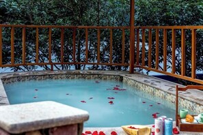 Un jacuzzi con barandilla de madera y un banco de piedra, rodeado de vegetación.