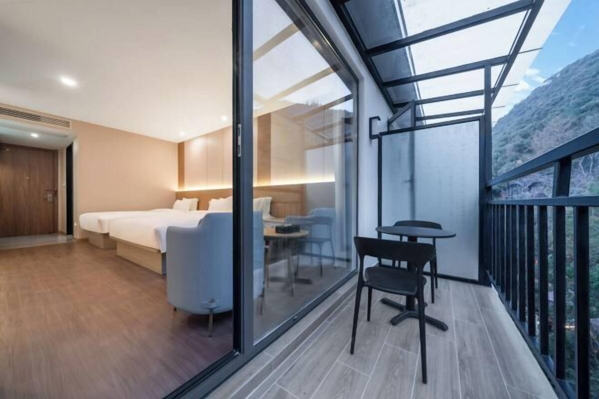 Quarto de hotel moderno com varanda, cama, área de estar e vista para o exterior.