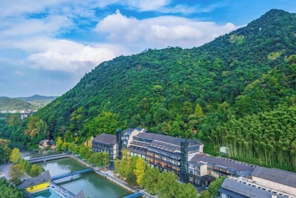A hotel with a river view, surrounded by lush greenery and hills. - Anji Meilin Resort (Anji)
