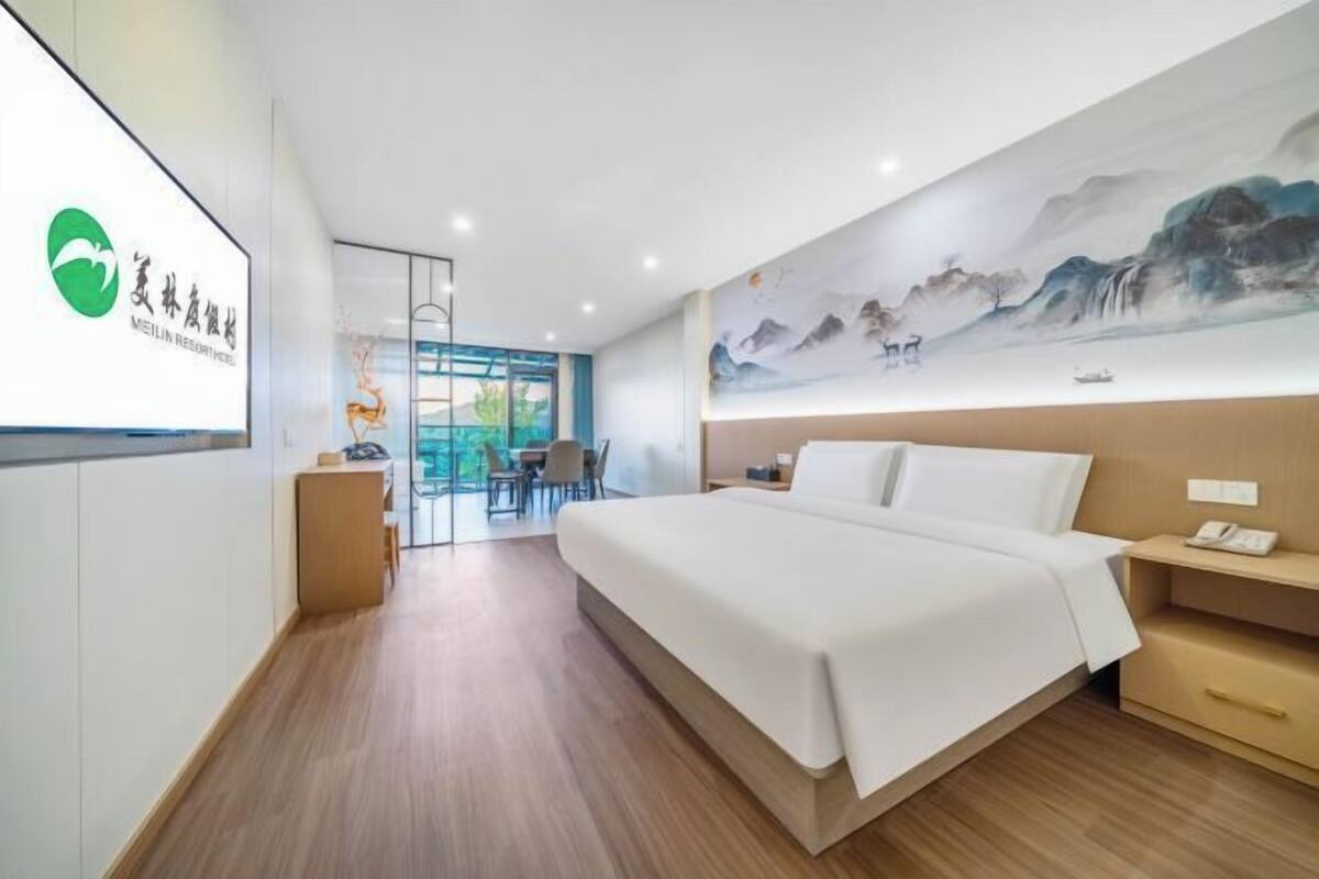 Quarto de hotel com cama, escrivaninha, cadeira, pintura na parede e vista para o exterior.
