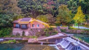 A house with a stone wall, a wooden deck, and a waterfall.