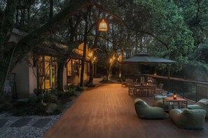 Una terraza de madera con mobiliario exterior y una cubierta, rodeada de árboles.