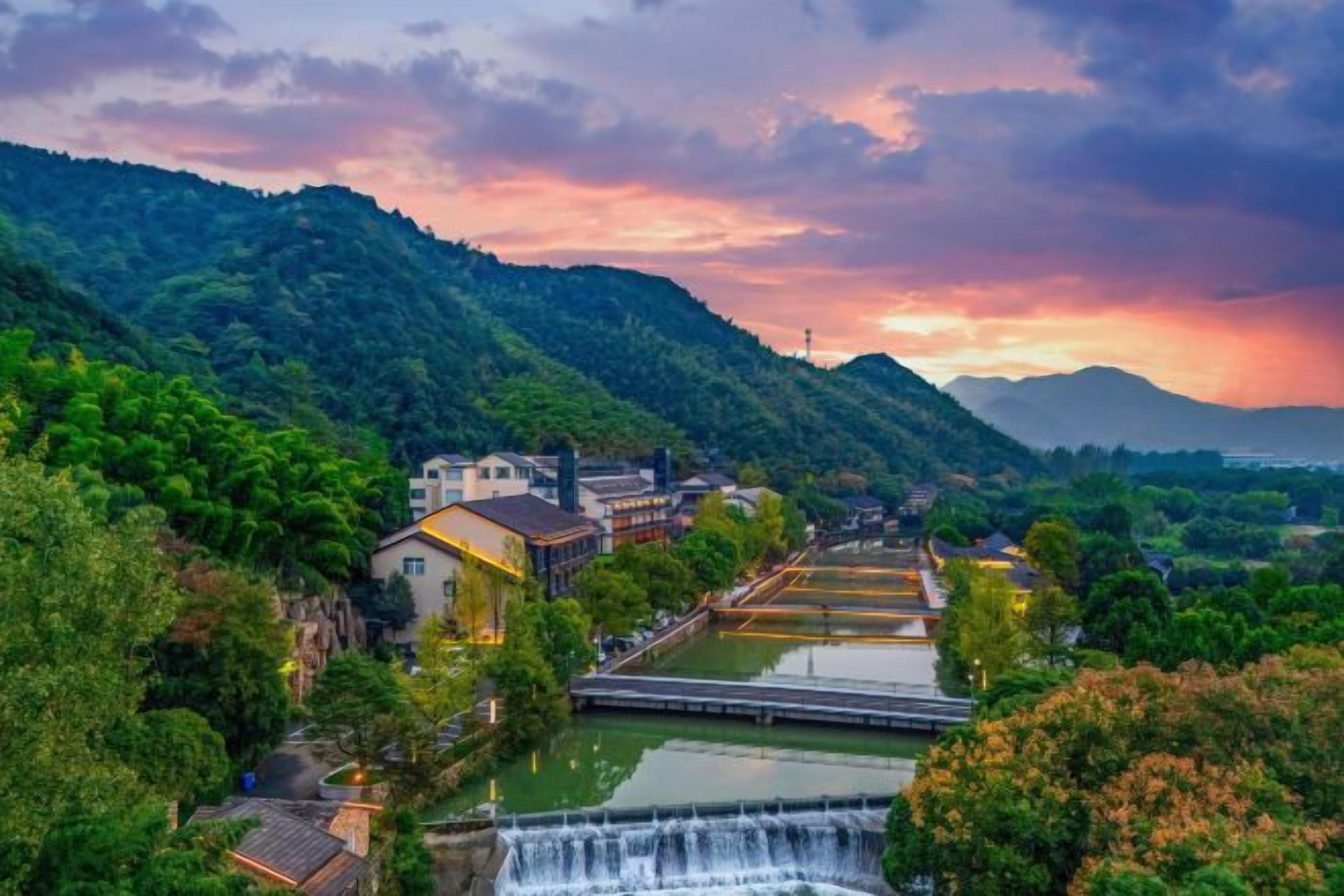 A riverside town with buildings, a waterfall, and a mountain backdrop.