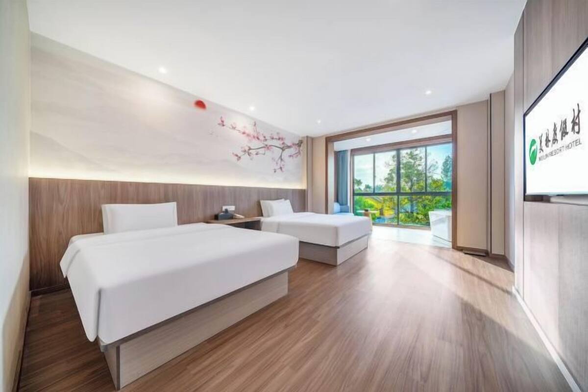 Quarto de hotel com duas camas, uma janela grande e vista para o verde.
