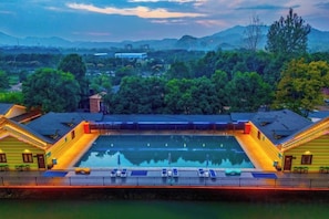 Una piscina con un deck circundante, un puente y vistas a un paisaje montañoso.
