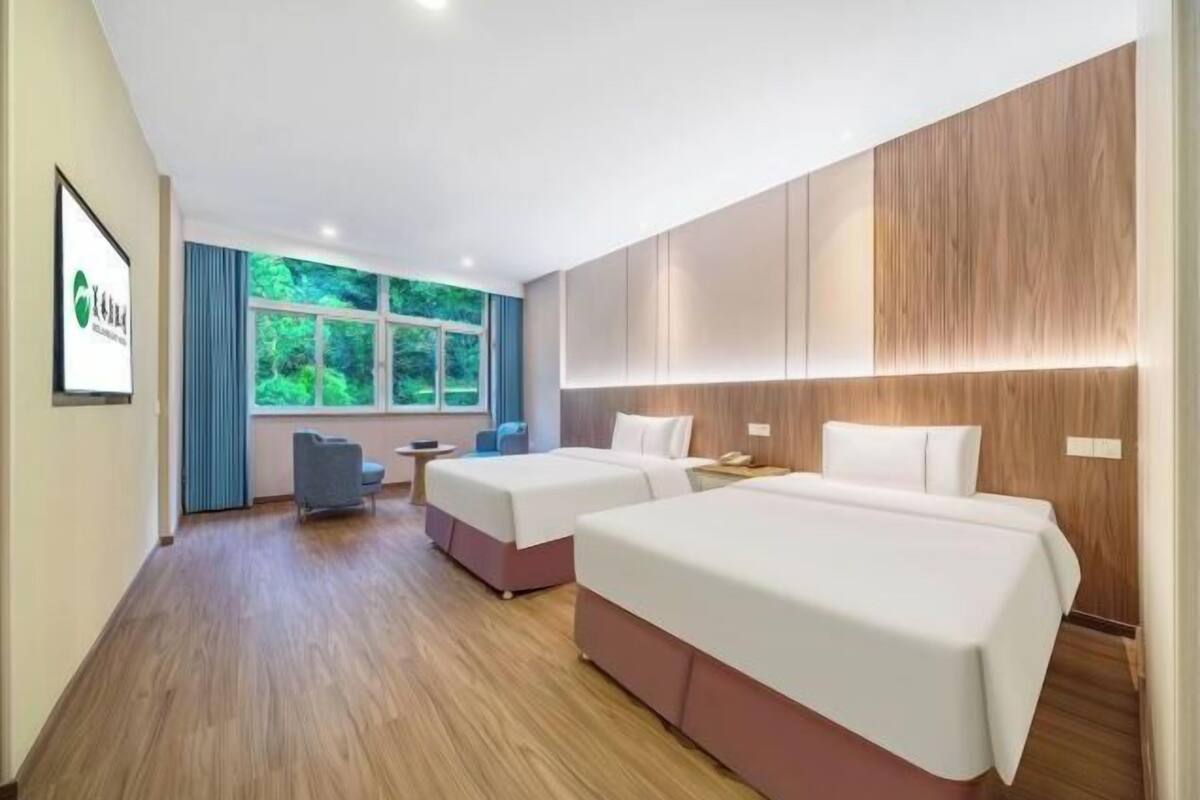 Quarto de hotel com duas camas, uma mesa de trabalho e vista para o verde.
