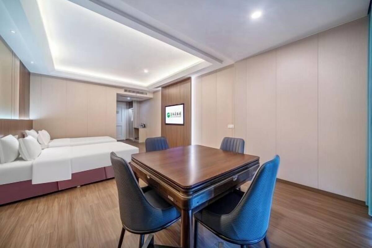 Quarto de hotel com mesa de jantar de madeira, cadeiras azuis, sofá branco e um espelho grande.