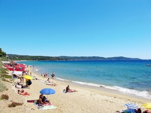 A beach with people sunbathing and swimming, red umbrellas, and a clear blue sky. - Le Domaine de la Baie by Interhome (Cavalaire)