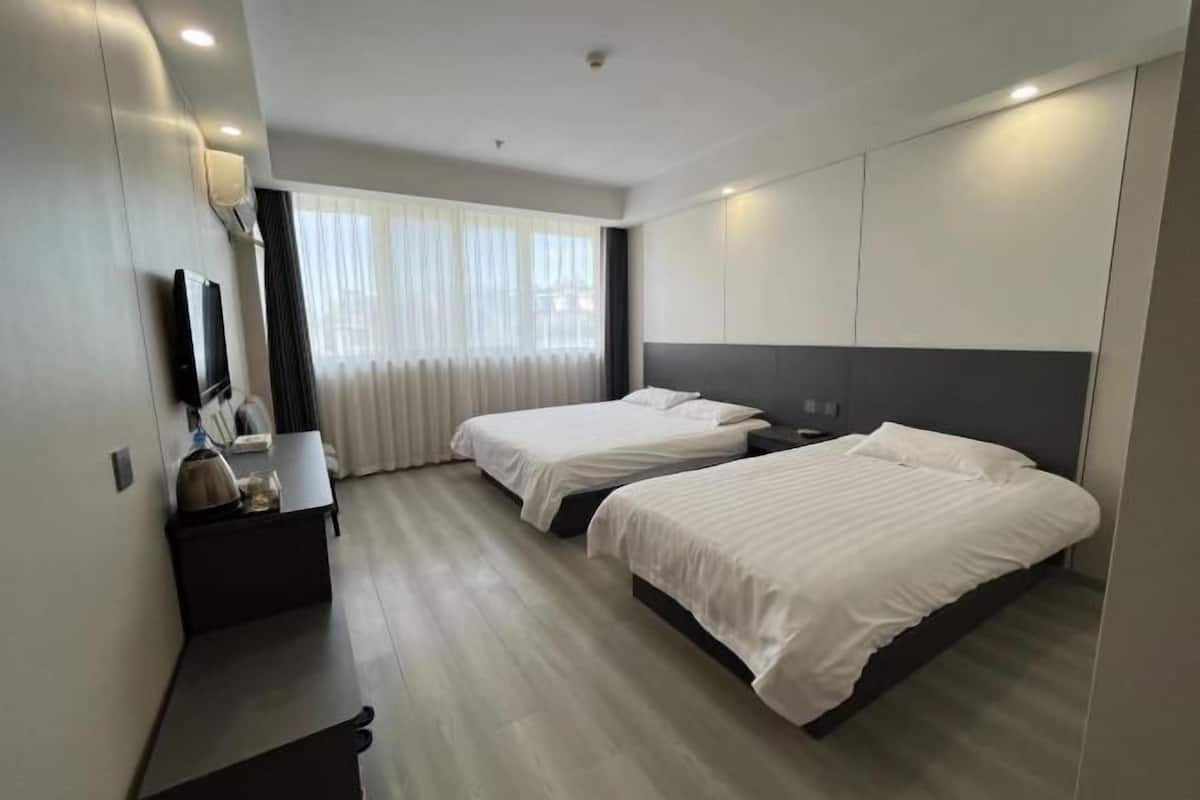 Une chambre d’hôtel moderne avec deux lits, un bureau, une télévision et une grande fenêtre avec des rideaux.