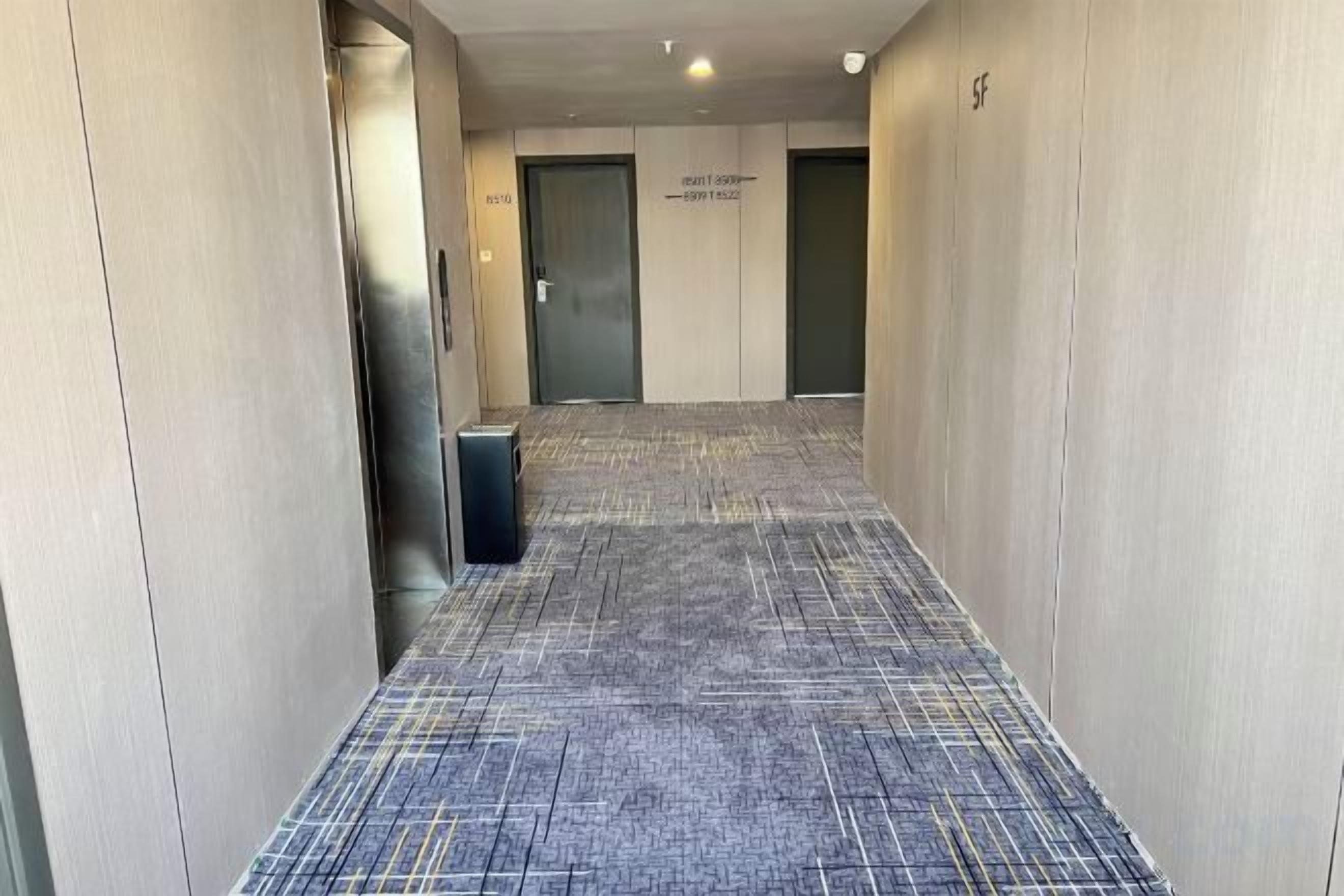 A corridor with carpeted flooring, a trash bin, and doors labeled 'SF' and 'SF 2'.