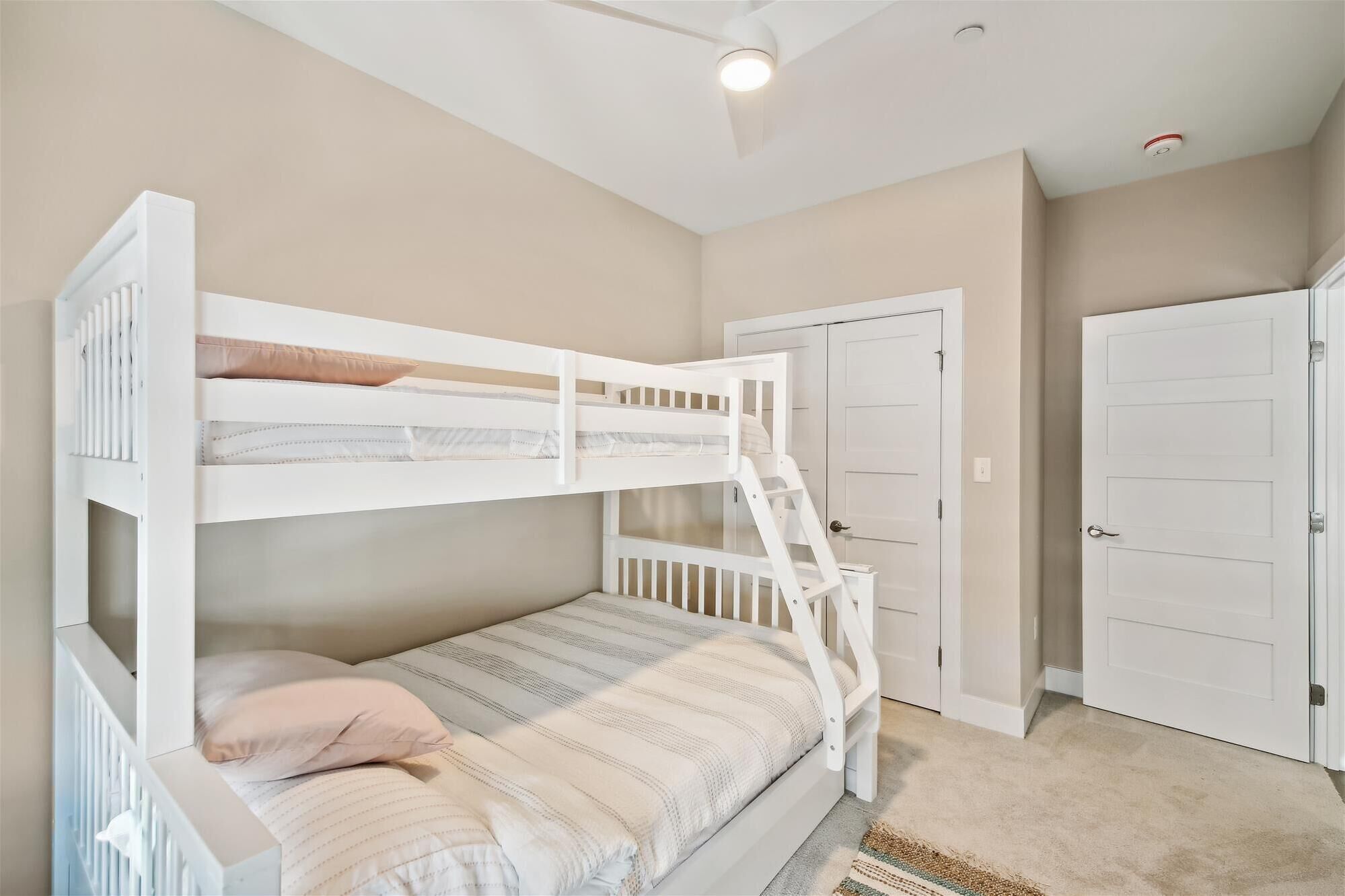 A bunk bed room with a ladder, a door, and a ceiling fan.