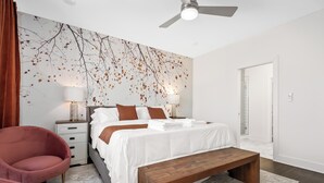 A modern bedroom with a large bed, bedside lamps, a wooden bench, and a wall mural. - Cozy Haven in Hermitage (Nashville)