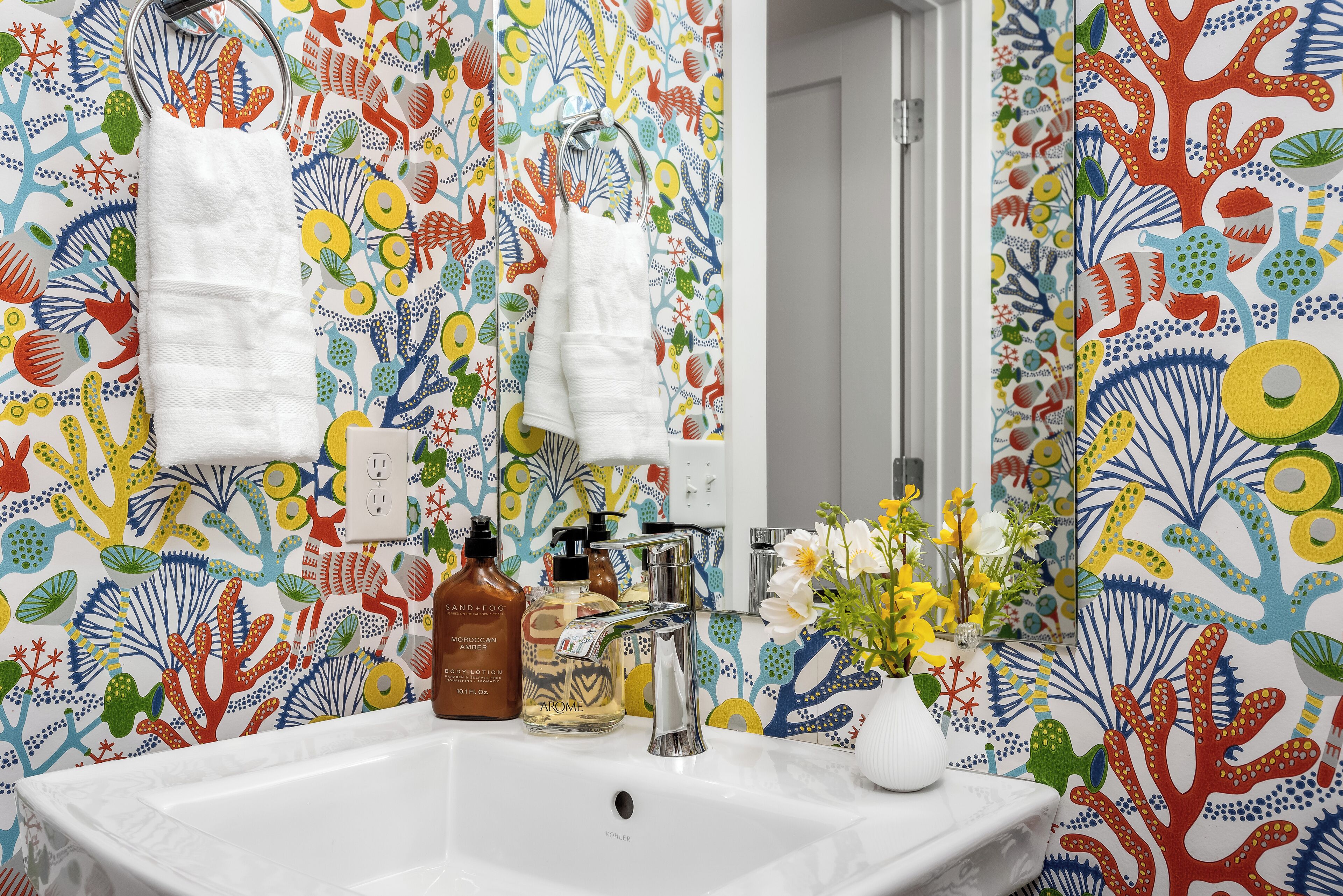 A bathroom with a colorful coral pattern wallpaper, a white sink, and a mirror.