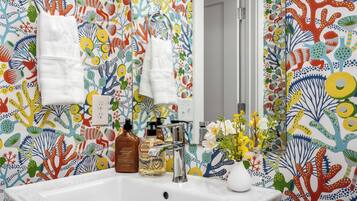 A bathroom with a colorful coral pattern wallpaper, a white sink, and a mirror.