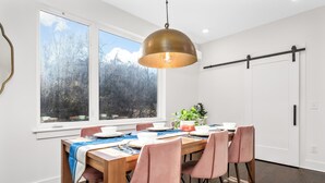 A dining area with a wooden table, pink chairs, and a large window with a view of trees and mountains. - Cozy Haven in Hermitage (Nashville)
