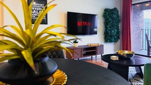 A modern living room with a black sofa, a round coffee table, a TV mounted on the wall, and a potted plant.