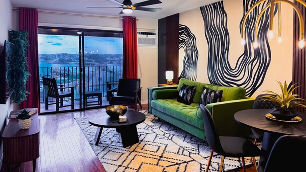 A modern living room with a green sofa, a round coffee table, and a view of a cityscape through large windows.