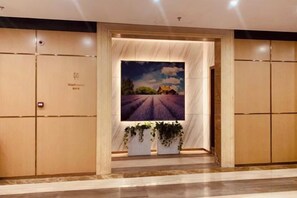A hotel entrance with a large floral display, a framed picture of a lavender field, and a sign indicating the washroom. - Xinken Hotel (Guangzhou)