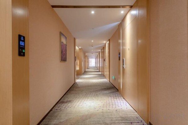 Un couloir d’hôtel avec un sol recouvert de moquette, des portes des deux côtés et un lecteur de cartes d’accès électroniques sur le mur gauche.
