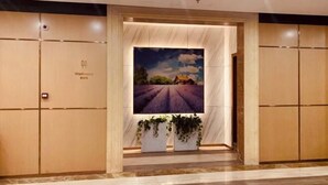Entrada de hotel con un cuadro grande enmarco de un campo de lavanda, paneles de madera y plantas en macetas.