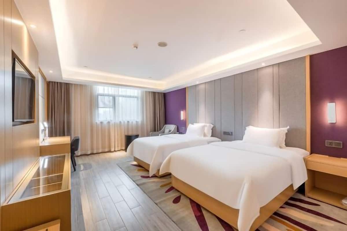 Habitación de hotel con dos camas, un escritorio, una silla y un amplio ventanal con cortinas.