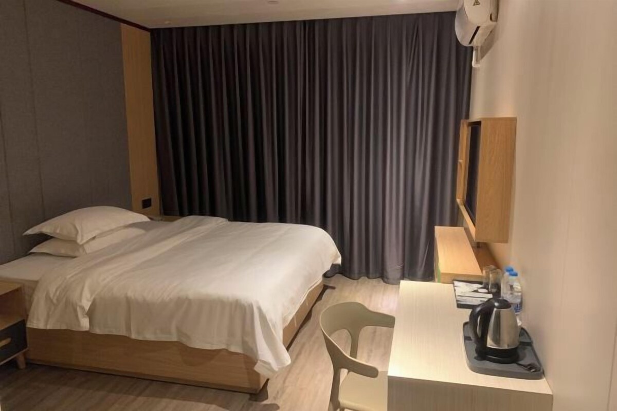 Habitación de hotel con cama, escritorio, silla, tetera y cortina.