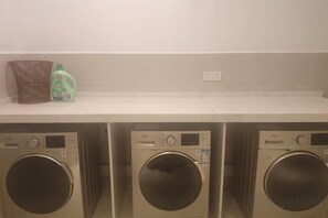 Un área de lavandería con tres lavadoras y un estante con una cesta y una botella.