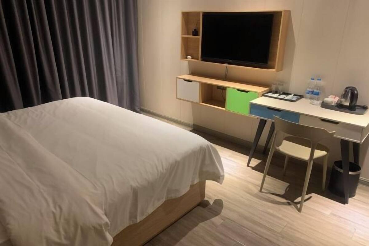 Una habitación de hotel con una cama, un escritorio con televisor de pantalla plana, una silla y un cesto de basura.