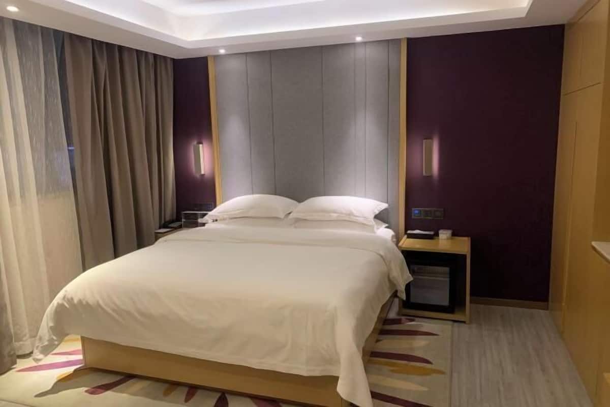 Una habitación de hotel con una cama, mesitas de noche, un escritorio y una cortina.