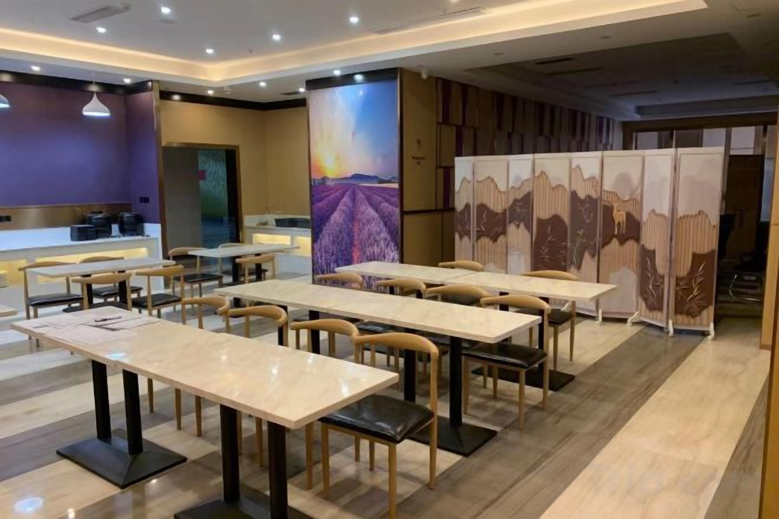 A hotel dining area with multiple tables and chairs, a reception desk, and a large decorative wall.
