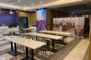 Un espace de restauration d’hôtel comprenant plusieurs tables et chaises, un comptoir de réception et un grand mur décoratif.