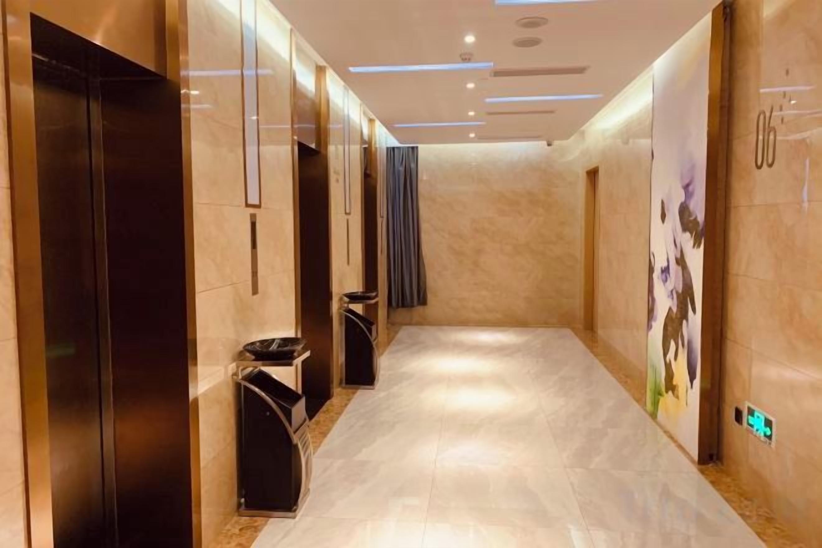 A hallway with elevators, trash bins, and a wall with a floral mural.