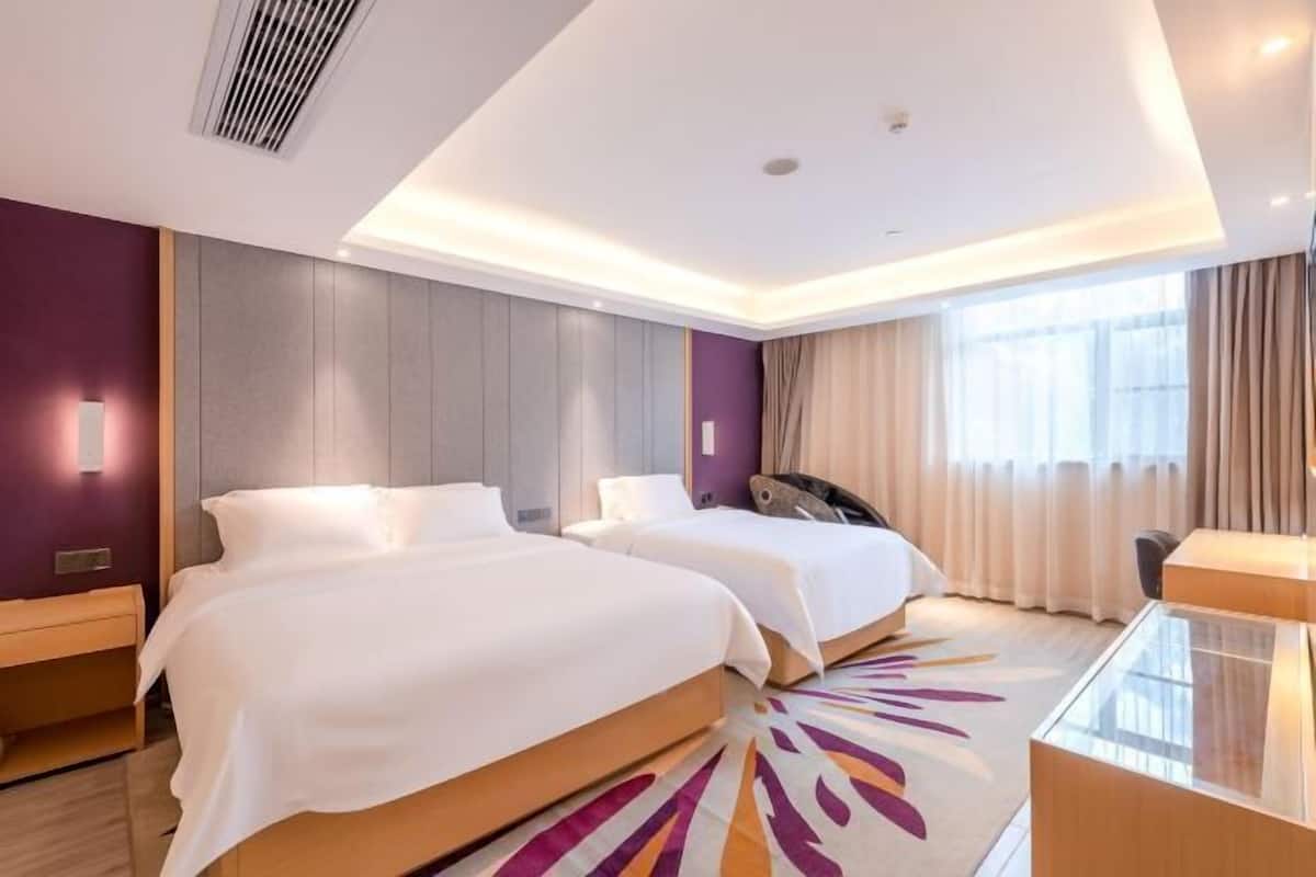 Habitación de hotel con dos camas, un escritorio, una silla y un amplio ventanal con cortinas.