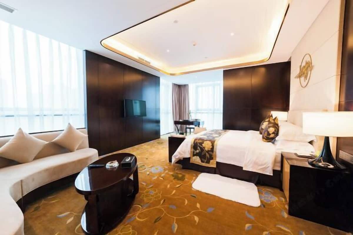 A modern hotel room with a sofa, a bed with a floral bedspread, a coffee table, and a TV.
