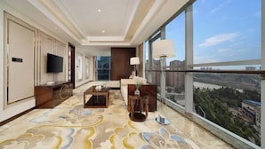 A hotel room with a large window, a flat-screen TV, a sofa, a coffee table, and a decorative rug. - Neijiang International Hotel (Wanda E-commerce Center) (Neijiang)